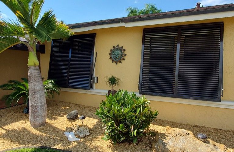 Tropical-style Bahama shutters partially open, providing both shade and storm protection for home windows.