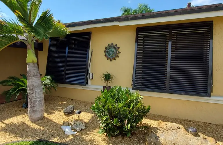 Tropical-style Bahama shutters partially open, providing both shade and storm protection for home windows.